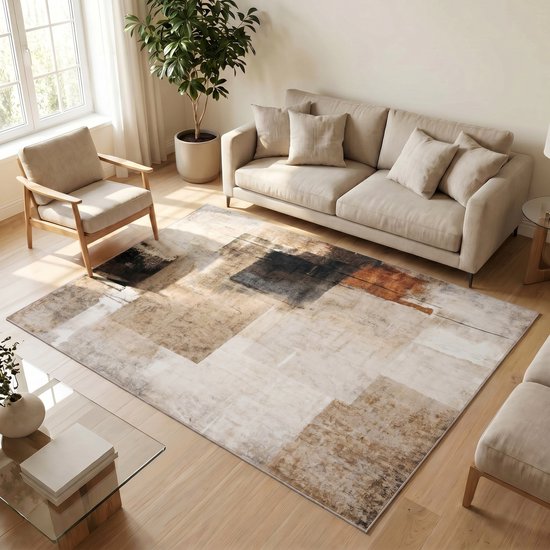 Un salon avec un tapis géométrique abstrait dans des tons beige, marron et noir, placé devant un canapé et une chaise beiges.