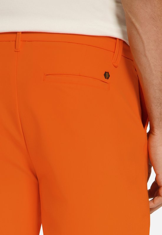 Sluiting van de achterzak van de oranje broek met een zwart logo.