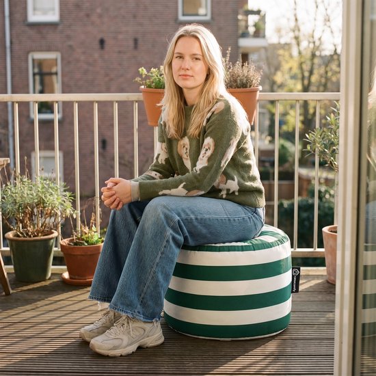 Vrouw op een groene en witte gestreepte poef op een balkon.