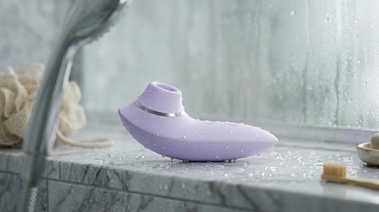 Lila luchtdruk vibrator met waterdruppels op een marmeren oppervlak in een douche.