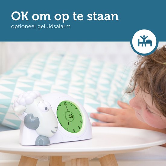 Een jong kind kijkt naar de ZAZU slaaptrainer in schaapvorm, die groen oplicht en 7:00 toont. Tekst: 'OK om op te staan'.