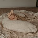 Pasgeboren baby slaapt op een beige voedingskussen, draagt een beige romper en een grote haarstrik.