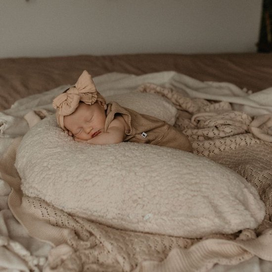 Pasgeboren baby slaapt op een beige voedingskussen, draagt een beige romper en een grote haarstrik.