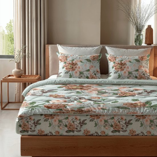 Een tweepersoonsbed met lichtgroen bloemenprint dekbed en bijpassende kussens. De houten ombouw van het bed is zichtbaar.