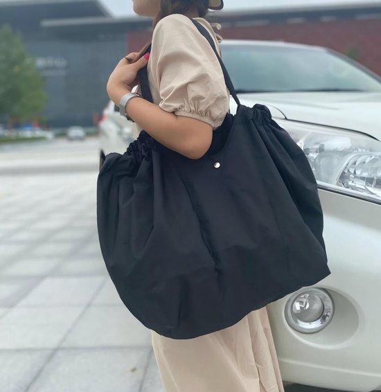 Femme portant un sac noir à fermeture à cordon, debout à côté d'une voiture blanche.