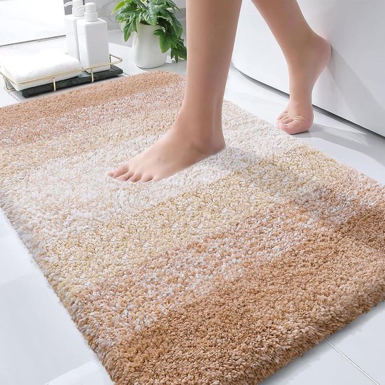 Pieds sur un tapis de bain doux et beige avec un dégradé de couleurs beiges et blanches, à côté d'une baignoire.