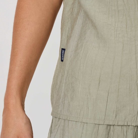Detail van een lichtgroene blouse met label 'SEASIDE' en een crinkle textuur.