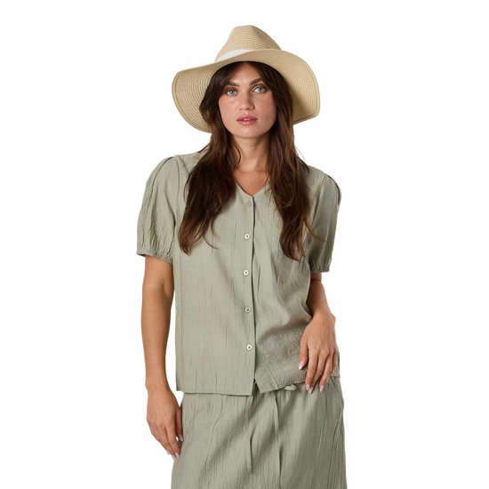 Vrouw draagt een lichtgroene blouse, een strooien hoed met wit lint en kijkt naar de camera.