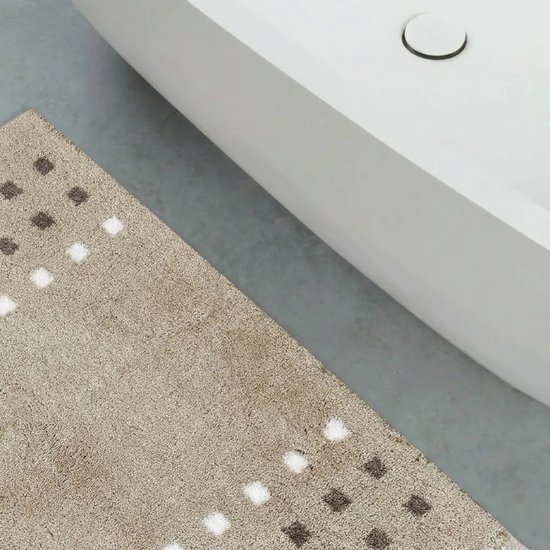 Beige badmat met bruin en wit vierkantjespatroon naast een witte badkuip.