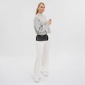 Model met grijze trui, witte broek en zwarte DKNY schoudertas.