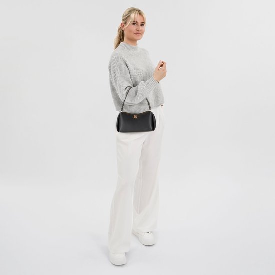 Model met grijze trui, witte broek en zwarte DKNY schoudertas.