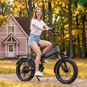 Grijze Maxtron elektrische vouwfiets gereden door een jonge vrouw in een bosrijke omgeving.