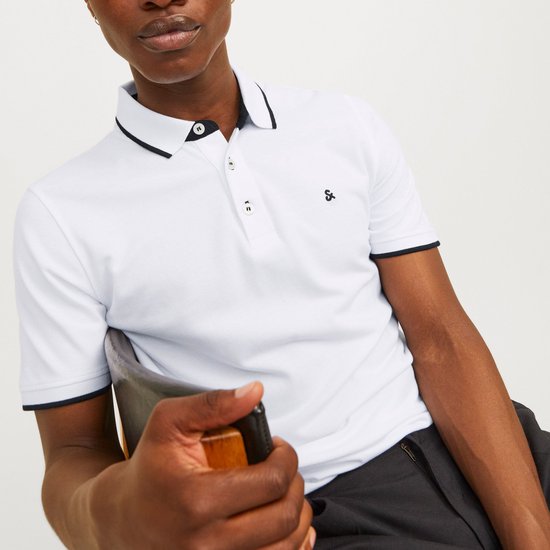 Model draagt een witte polo met zwarte bies bij kraag en mouwen. Zwarte broek.