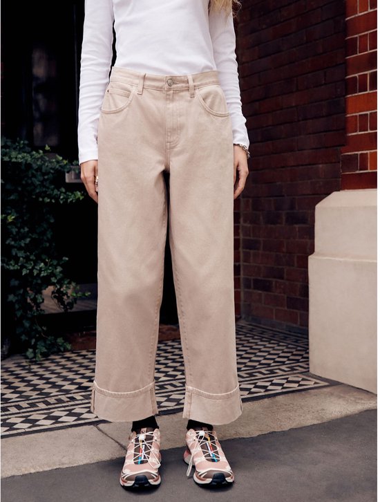 Model dat een beige wijde spijkerbroek draagt met omgeslagen boorden en roze sneakers.