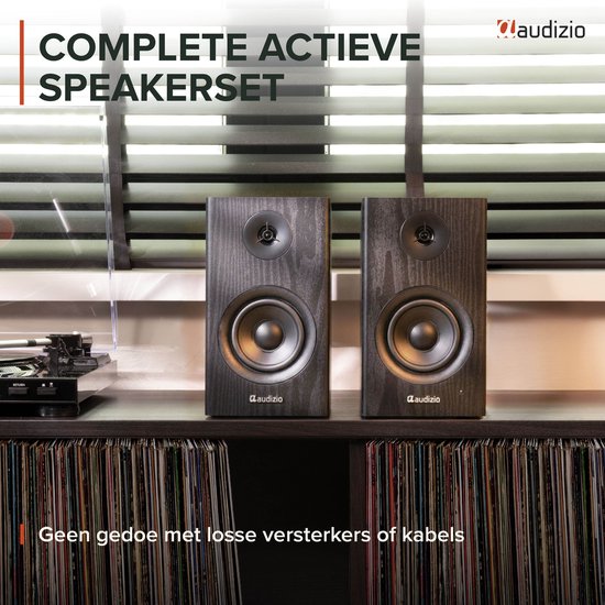 Twee zwarte houten boekenplank speakers op een donker dressoir, met een vinyl platenspeler en platen eronder.