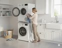Een vrouw laadt wasgoed in een droger die boven op een wasmachine staat, op een wit wasmachine-opbouwmeubel.