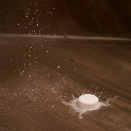 Een witte douchetablet ligt op een houten vloer, met water en zeep eromheen.