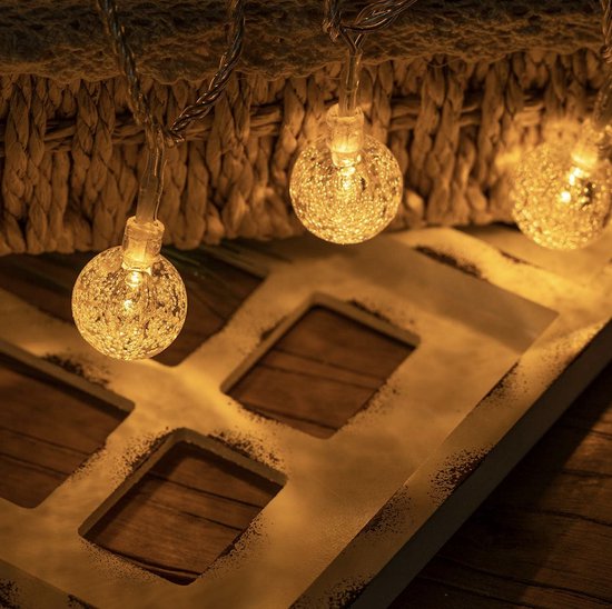 Trois ampoules rondes et plissées avec effet filament d'une guirlande lumineuse, suspendues devant un panier tressé.