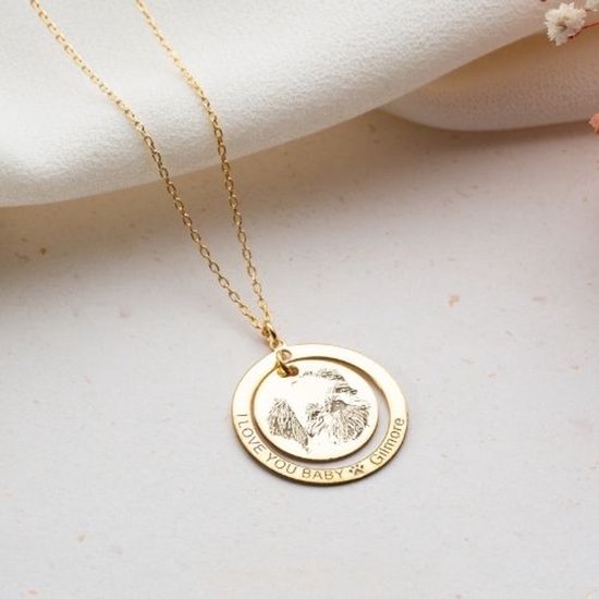 Gouden ketting met dubbele hanger. De bovenste hanger is een gouden cirkel met de tekst 'I LOVE YOU BABY' en een pootafdruk. De onderste hanger is een ronde medaillon met een gegraveerde afbeelding van een hondenkop.