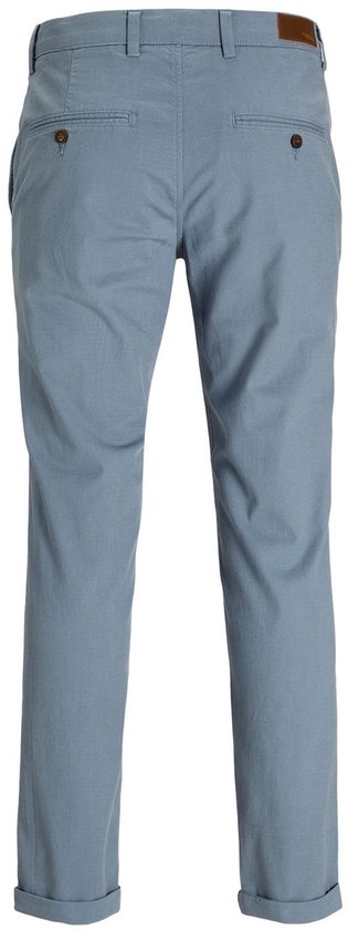 Achterkant van een blauwgrijze chino met een ruitpatroon, bruine label en knopen op de achterzakken.