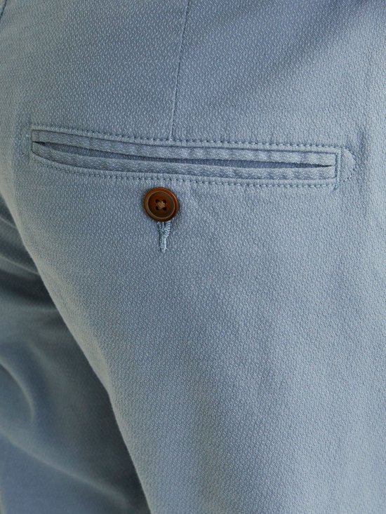 Detail van de achterzak van een blauwgrijze chino met een knoop en ruitpatroon.
