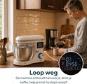 Crème keukenmixer op aanrecht, man giet koffie. Dichtbij digitaal display toont timer.