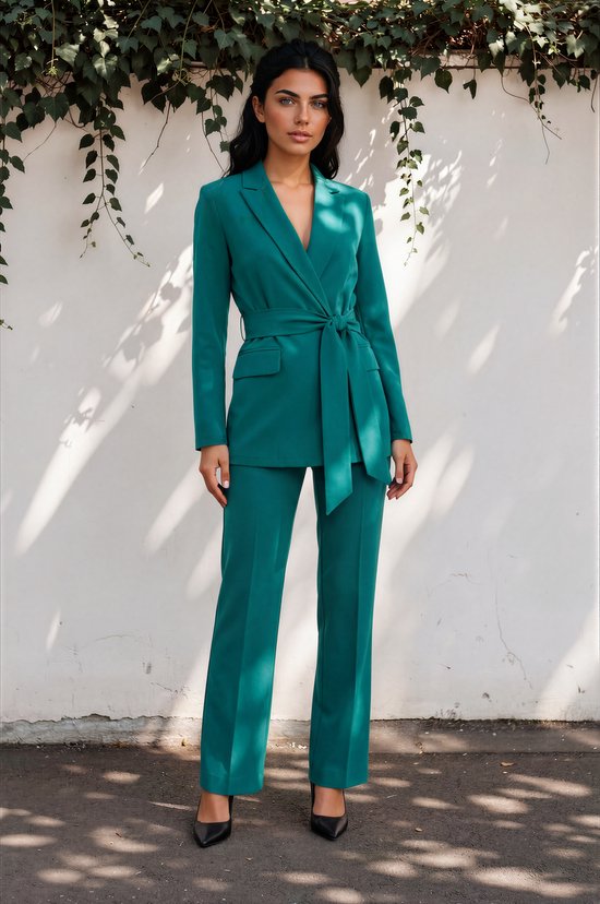 Model in een petrolkleurige blazer met strikceintuur en wijde pijpen broek. De blazer is lang met klepzakken.