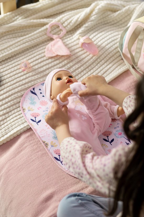 Een baby-pop in roze kleertjes krijgt een sokje aan op een aankleedkussen met bloemen.