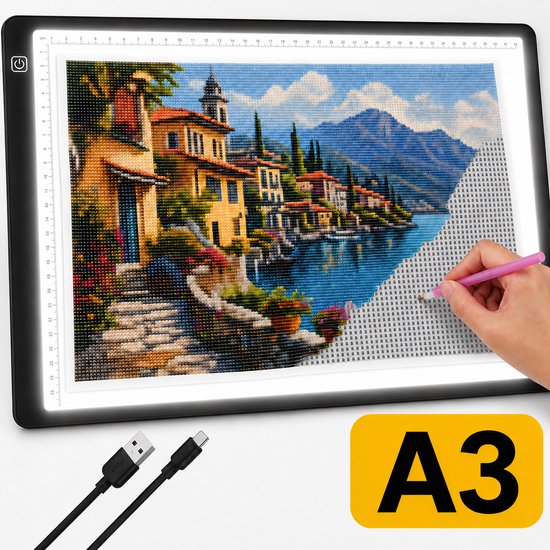 A3 lichtbord met een gedetailleerde afbeelding van een Italiaans dorp aan een meer, halverwege diamant painting. Een hand met een roze pen is bezig.