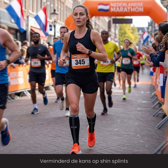 Vrouw met zwarte R2B compressiekousen en oranje schoenen rent tijdens een marathon.