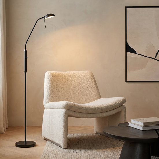 Zwarte staande leeslamp naast een crème fauteuil in een modern ingerichte woonkamer.