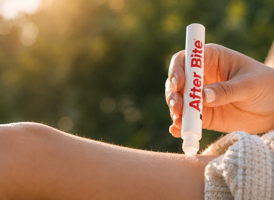 Een hand wordt met de After Bite pen gebruikt op een arm. De pen is wit met rode tekst.
