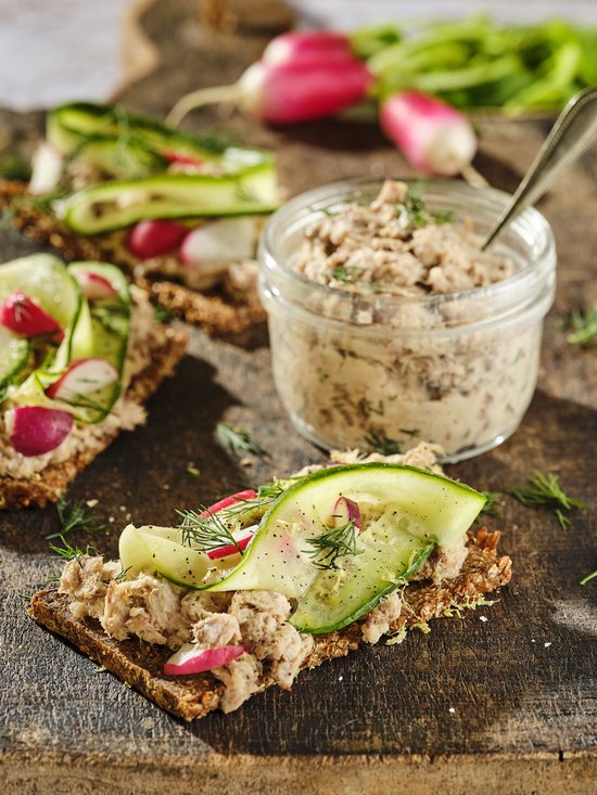 Twee toastjes belegd met visspread, komkommer, radijs en dille, naast een potje met visspread.