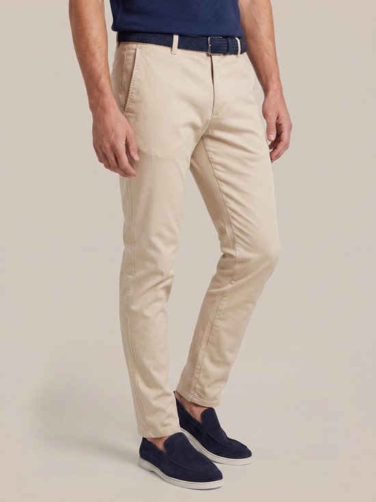 Man in een donkerblauw poloshirt en lichtbeige chino, staand.