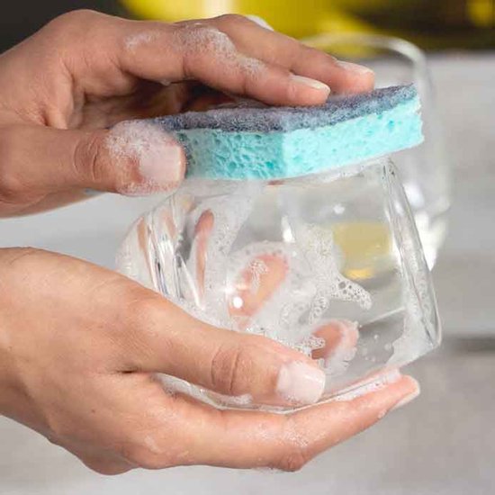Mains lavant un verre avec une éponge à récurer bleue.