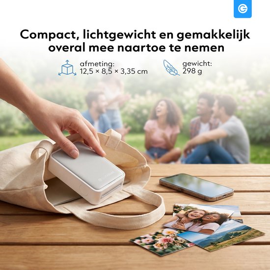 Een hand plaatst een compacte, witte Silvergear mini fotoprinter in een stoffen tas. Een smartphone en meerdere foto's liggen op de tafel.