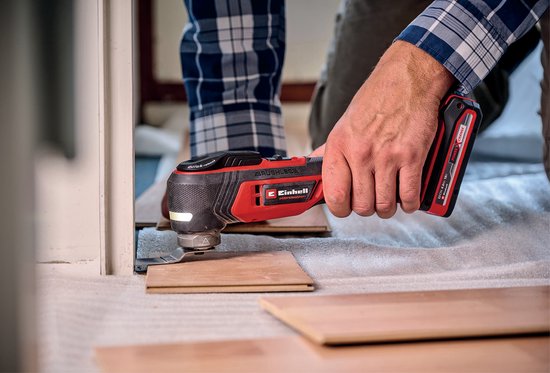 Man met rood-zwarte multitool werkt aan een houten vloer.