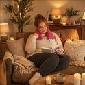 Een vrouw leest een boek met een rood kersenpitkussen om haar nek.