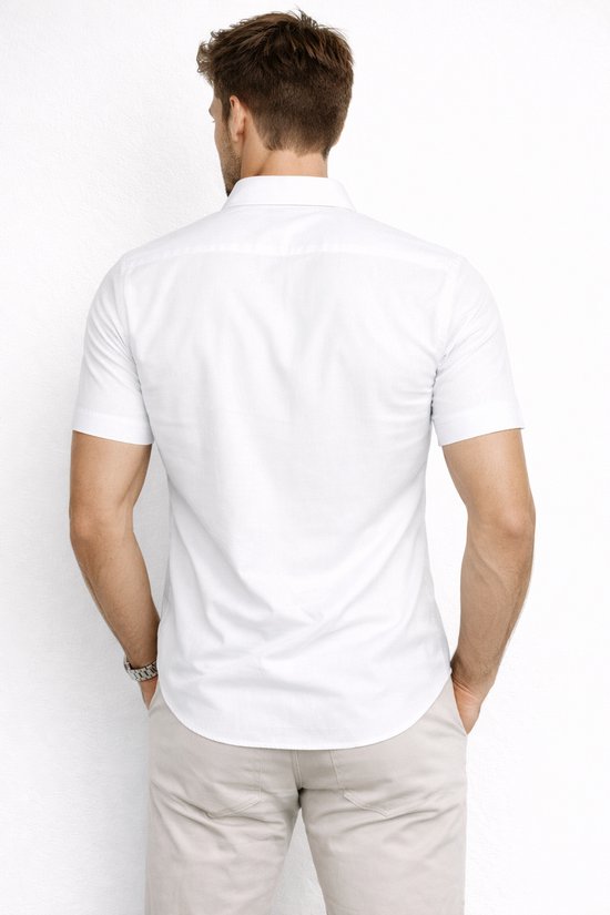 Man draagt achterkant van een wit kort T-shirt, handen in zakken. Bruine riem en horloge zichtbaar.