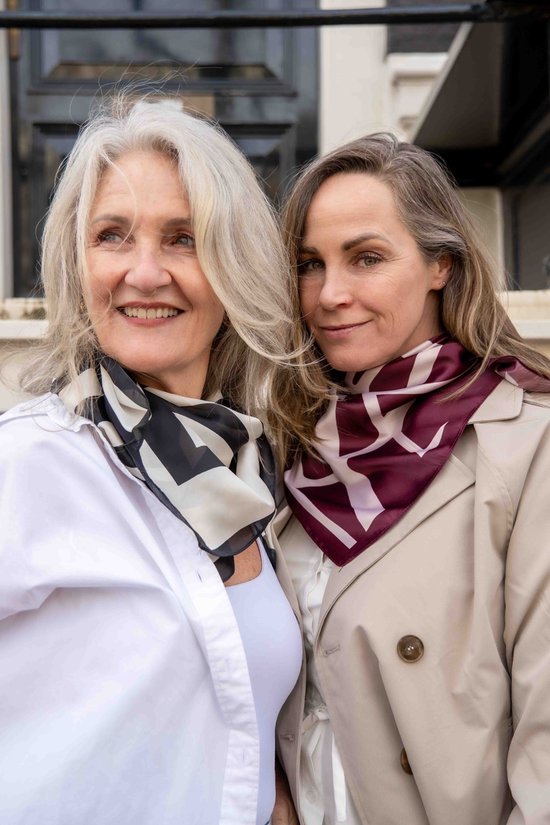 Twee vrouwen met sjaals met bordeauxrode en beige logo-print. De ene sjaal heeft een zwarte en witte print.