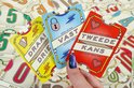 Hand die een rode 'TWEEDE KANS' kaart vasthoudt, met twee hartjes. Naast de rode kaart liggen een gele 'DRAAI DRIE' en blauwe 'VAST' kaart.