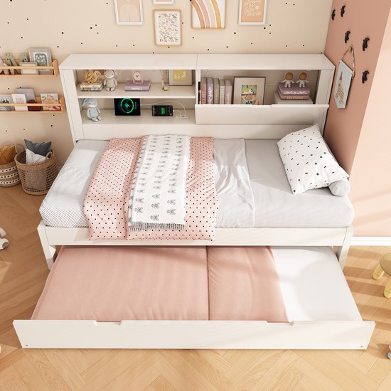 Wit kinderbed met een uitgetrokken uitschuifbed en opbergruimte in de rugwand. Roze en witte dekens.
