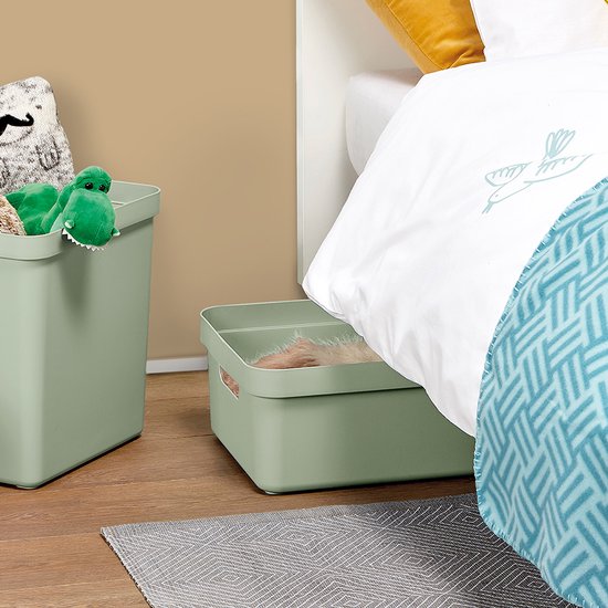 Twee lichtgroene opbergboxen naast een bed, een gevuld met een dinosaurusknuffel, de ander met een deken.