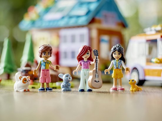 Drie LEGO Friends poppetjes met een gitaar, kat, konijn, puppy en salamander op een groene ondergrond.