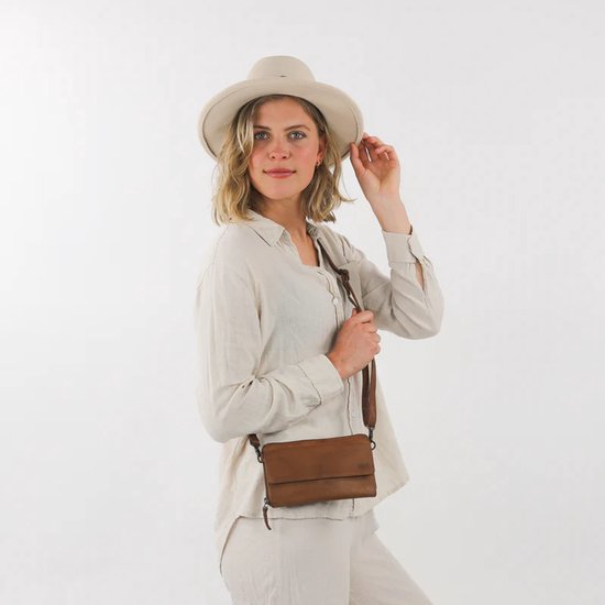 Model met een lichtbruine leren schoudertas, cognac kleur, met een brede riem en een hoed.