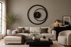 Horloge murale moderne en métal noir avec aiguilles dorées, au-dessus d'un canapé modulaire beige avec divers coussins.