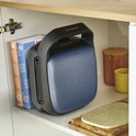 Een donkergrijs Tefal wafelijzer met blauw bovendeel, staat opgeborgen in een kast naast twee Tefal dozen.