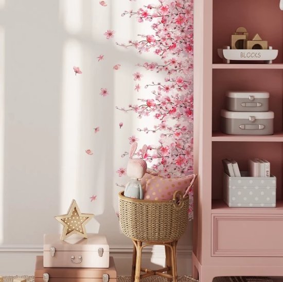Roze bloesemtakken langs een muur, met losse bloesems en een mand met knuffels en kussens op de grond.