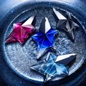 Vier Mugler Angel Stellar sterflacons in blauw, roze, lichtblauw en grijs, op een bed van blauwe glitter.