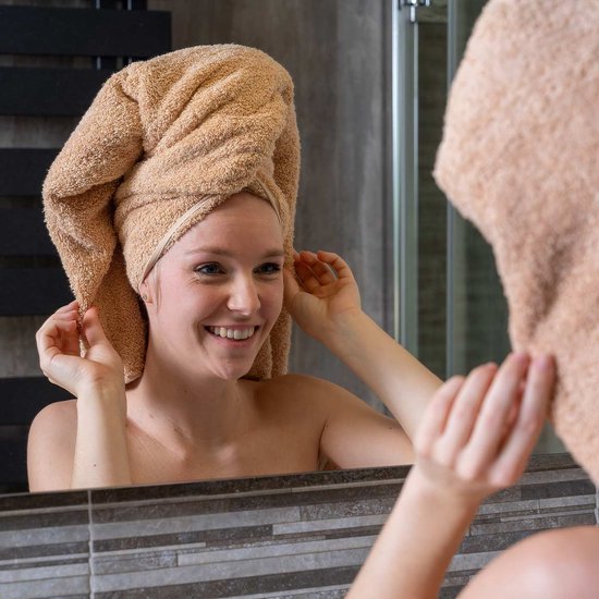 Femme joyeuse avec une serviette couleur sable sur la tête dans la salle de bain.
